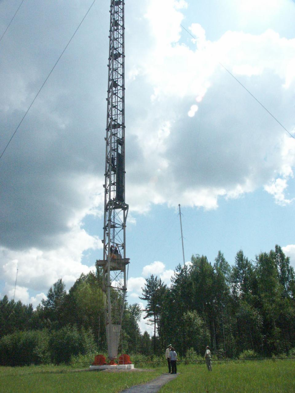 Close view of a lattice mast base with people standing in the grass for scale