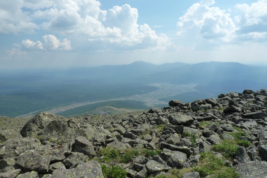 Summer view from the rocky upper slope of Kosvinsky Kamen down to a broad valley with a river and a pale mining scar